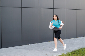Young woman with fit body jumping and running against dark wall background. Female model in...