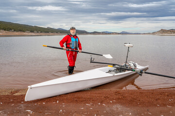 senior rower is rigging his rowing shell on a shore of Carter Lake in northern Colorado in winter...