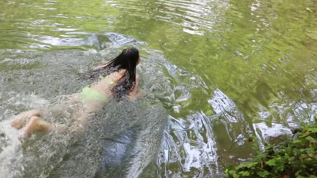 Girl in swimwear swims in cold water of mountain river at summer day, slow motion