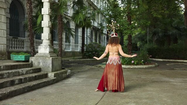 Woman dances belly dance with chandelier on head near building of sanatorium, 