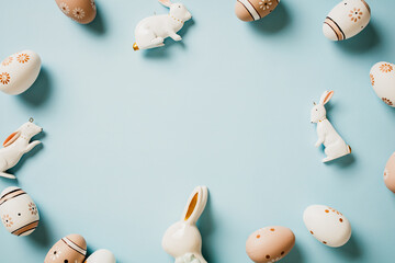 Frame of floral painted Easter eggs with bunny rabbits on pastel blue background. Top view. Flat...