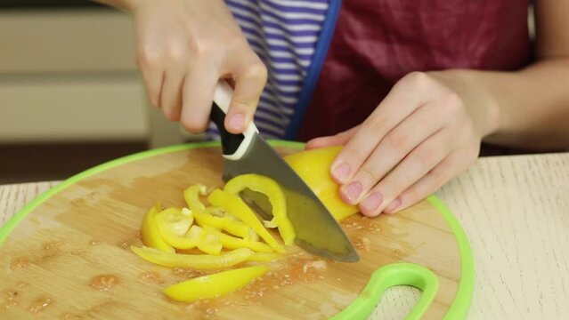 Child hands cut sweet pepper on cutting board on table in kitchen