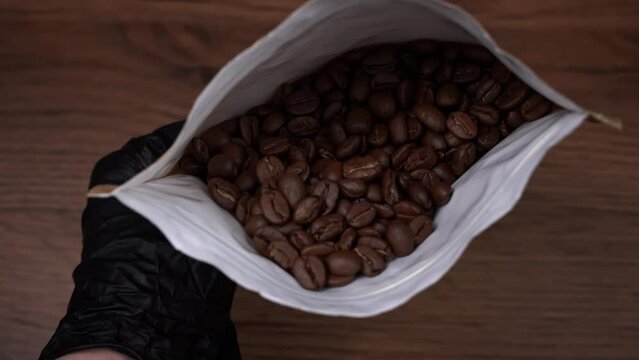 Coffee beans in craft packaging in human hands. Roasted aromatic brown coffee beans. Dark roast Arabica coffee beans falling. Roasted aromatic coffee.