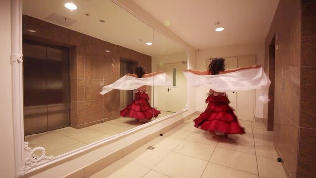 Pretty woman in costume with scarf belly dances in hall with big mirror