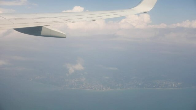 Wing of flying aircraft, clouds and sea coast, view from airplane