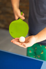A man is playing ping pong. He holds a white ball and a green racket in his hands. Table tennis....