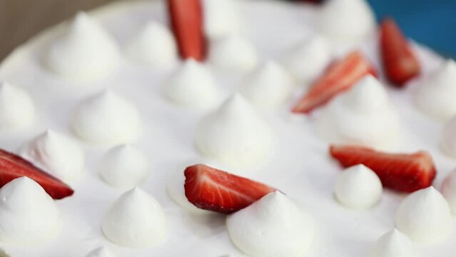 Hand puts strawberry pieces in white sweet whipped cream, close-up