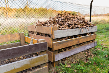 A composter made of wooden boards filled with dry leaves.