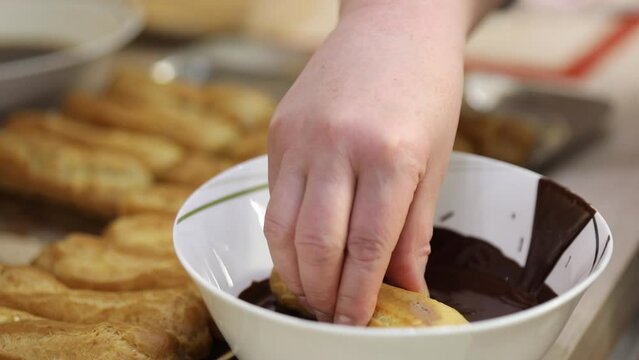 Hand dunks eclair into chocolate, close up, slow motion