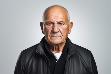Elderly man wearing a leather jacket. Studio shot against a grey background.