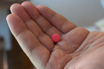 Close-up of a single pink pill in the center of an open hand