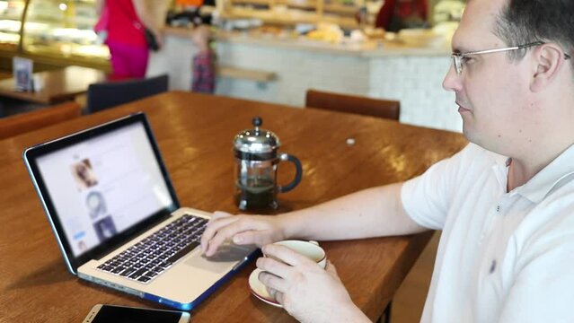 Man visits ebay site on laptop in cafe (with chromakey), smartphone, tea are on table, slow motion