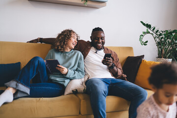 Cheerful multiethnic couple sitting on couch while enjoying time together