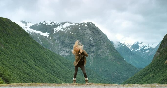 Hiking, nature and happy woman by mountains dancing on snow green hills outdoors for freedom. Wellness, dancer or excited female tourist jumping in celebration of fun adventure alone in Stryn, Norway