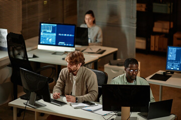 High angle view at IT developers office with people working at night and using computers, copy space