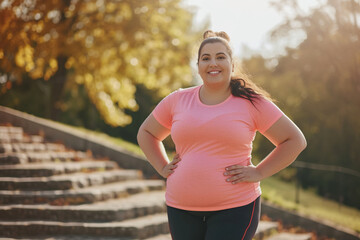 Happy young overweight woman having active fitness workout outside. Fat chubby plump lady in sports clothes standing on stone staircase in beautiful city park, doing lateral bend exercise and smiling