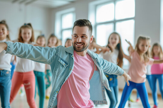 Male friendly choreographer helping his students girls in doing dance exercises in studio. Happy kids doing dance workout. Children training in choreography class, learning modern dances. © wolfhound911