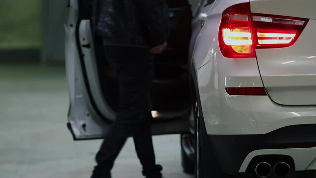 Man wearing dark clothes and white shoes gets in car on dark underground parking