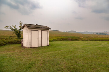Fototapeta na wymiar His and Hers Outhouses in a Green Field in Fort Abraham Lincoln State Park, Mandan, North Dakota on a Cloudy, Stormy Day
