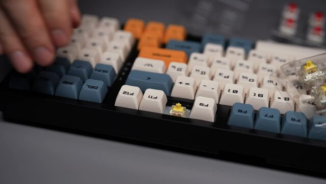 Close-up hands of unrecognizable man assemble wireless mechanical keyboard with colorful switches sitting at desk in dark room with cozy light. Push buttons digital keyboard unit, slow motion.