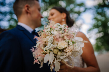 Valmiera, Latvia - July 7, 2023 - Close-up of a bride and groom facing each other, bride holding a bouquet, with a blurred green background.