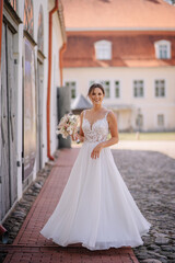 Obraz premium Valmiera, Latvia - July 7, 2023 - Bride in a flowing white dress with a bouquet, walking on a cobblestone street, buildings in background.