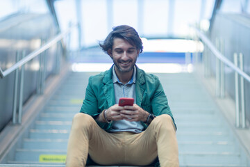 View of young man sitting down using a smartphone at indoor space with a blurred view landscape in...