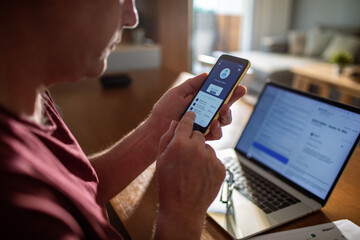 Back view of a man using bank smartphone app at home