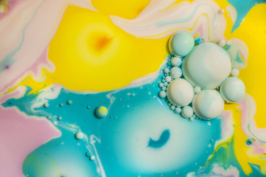 A vibrant abstract of swirling yellow, blue, and pink ink colors with white bubbles creating a marbled effect underwater