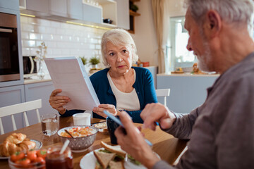 Elderly couple reading bills at the kitchen table