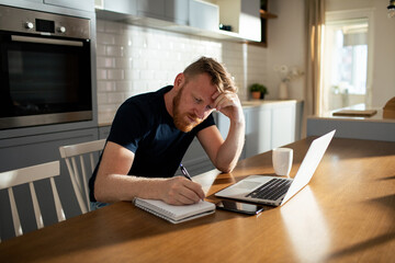 Contemplative man working from home with his laptop and notebook