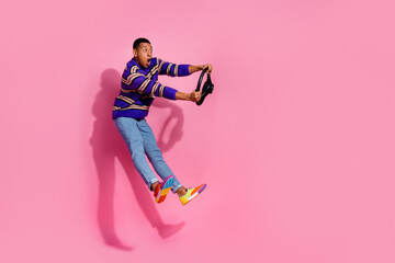 Full body photo of attractive young man jump dangerous driving wear trendy purple striped clothes isolated on pink color background
