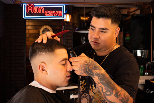 Barber trimming hair of client with clipper in barbershop