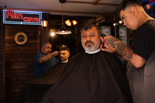 Barber trimming hair of client with clipper in barbershop