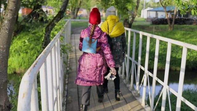 Two girls walks with bags by bridge at summer day. Slow motion