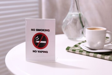 No Smoking No Vaping sign and cup of coffee on white table indoors