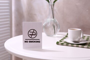 No Smoking sign and cup of coffee on white table indoors