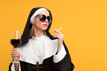 Woman in nun habit holding glass of wine and cigarette against orange background. Space for text - obrazy, fototapety, plakaty