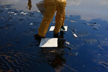 Professional team and volunteer wearing PPE clean up dirty of oil spill on the beach,  oil slick...