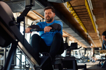 Mature athletic man exercising on rowing machine in gym.