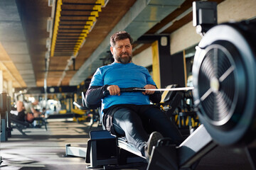 Middle aged athlete using rowing machine while working out in gym.