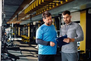 Mature man and his personal trainer making exercise plan for gym workout.