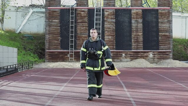 Fireman in fireproof suit puts off red helmet and walks from fire tower on training test area