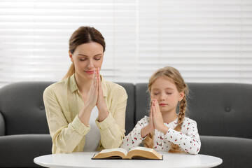 Girl and her godparent praying over Bible together at table indoors