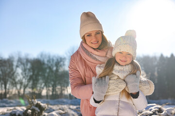 Family portrait of happy mother and her daughter in sunny snowy park. Space for text