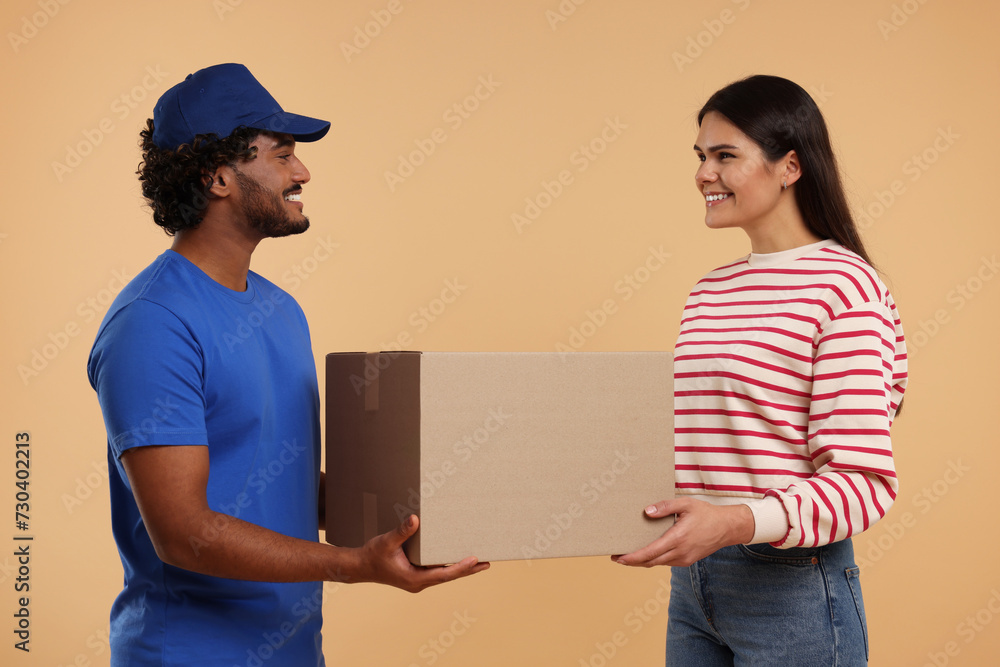 Poster Smiling courier giving parcel to receiver on light brown background