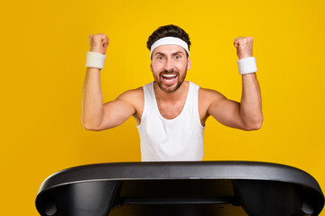 Photo of lucky cheerful guy activewear running treadmill rising fists screaming yes isolated yellow...