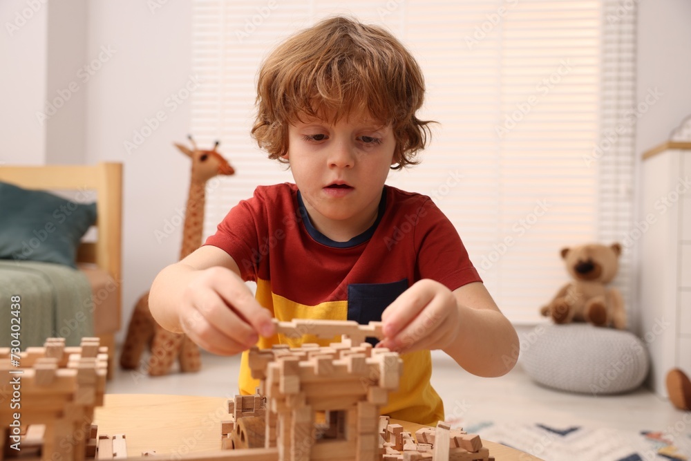 Poster Little boy playing with wooden entry gate at table in room. Child's toy