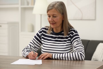Senior woman signing Last Will and Testament at wooden table indoors