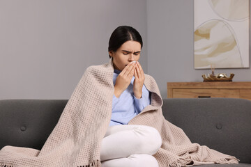 Woman coughing with tissue on sofa at home. Cold symptoms